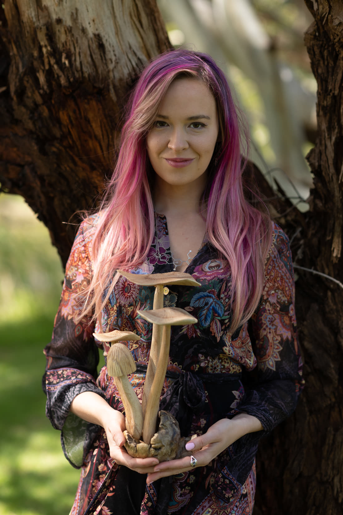 Melissa Warner standing among trees in a natural landscape, holding a small carved offering